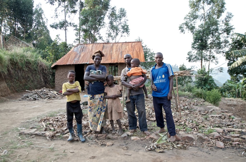 A Hutu family from the Bibotobolo village, in the Masisi territory, in the ruins of their former home, which was destroyed during the interethnic violence at the end of 2012. Having spent several months in a camp for displaced people, they have just finished building a new home (behind them), specifically by reusing the charred corrugated iron sheets from their former lodgings. Bibotobolo, Masisi, June 2013.